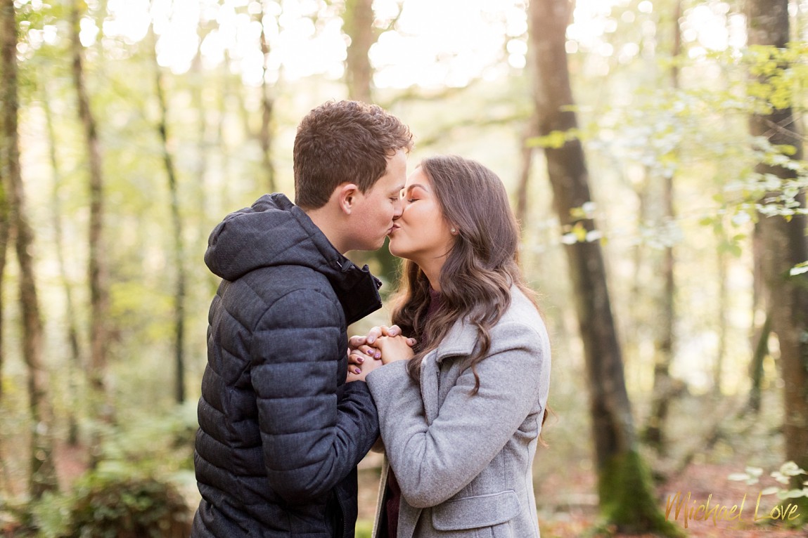 Engaged couple kissing in woods at sunset