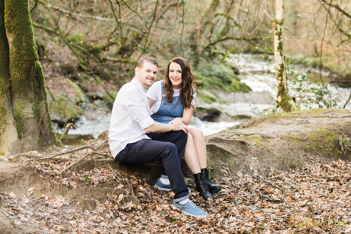 Engaged couple sitting on ground beside river