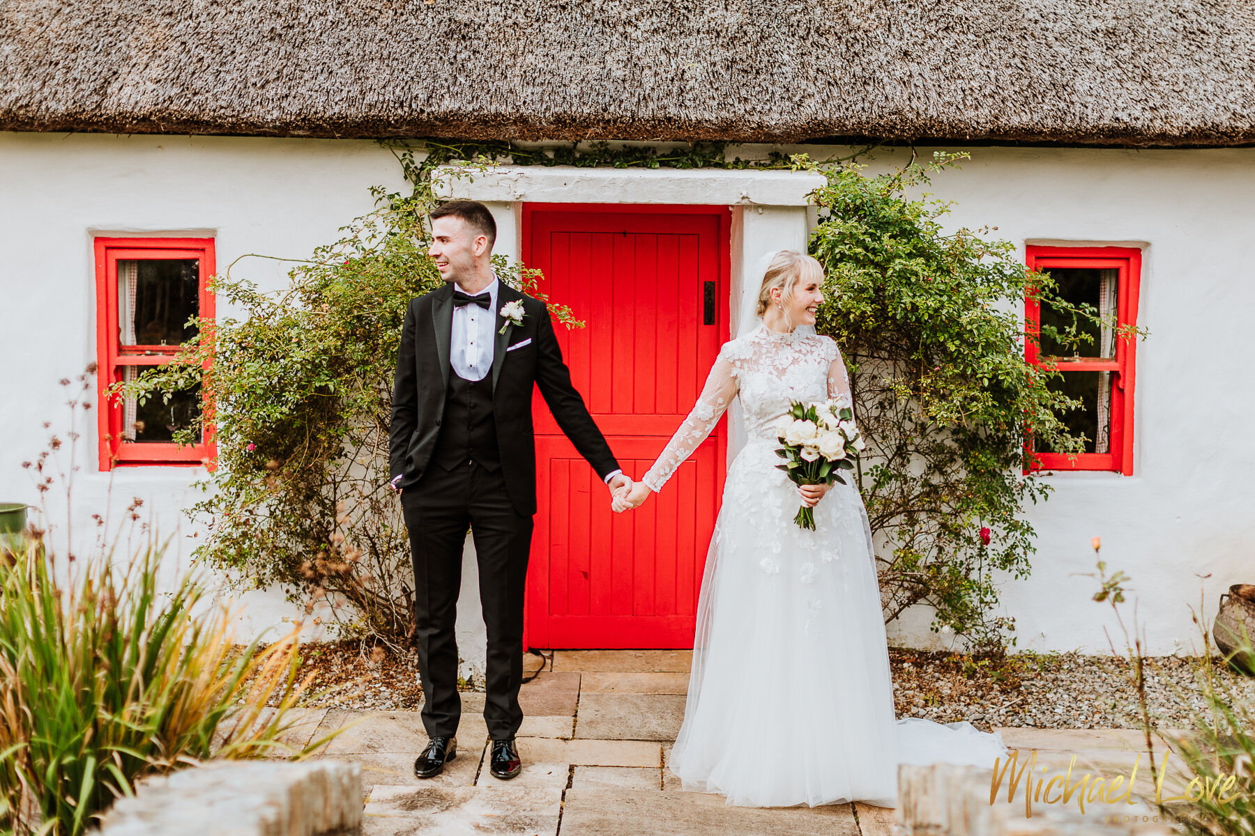 Bridal couple outside cottage with thatched roof & red door